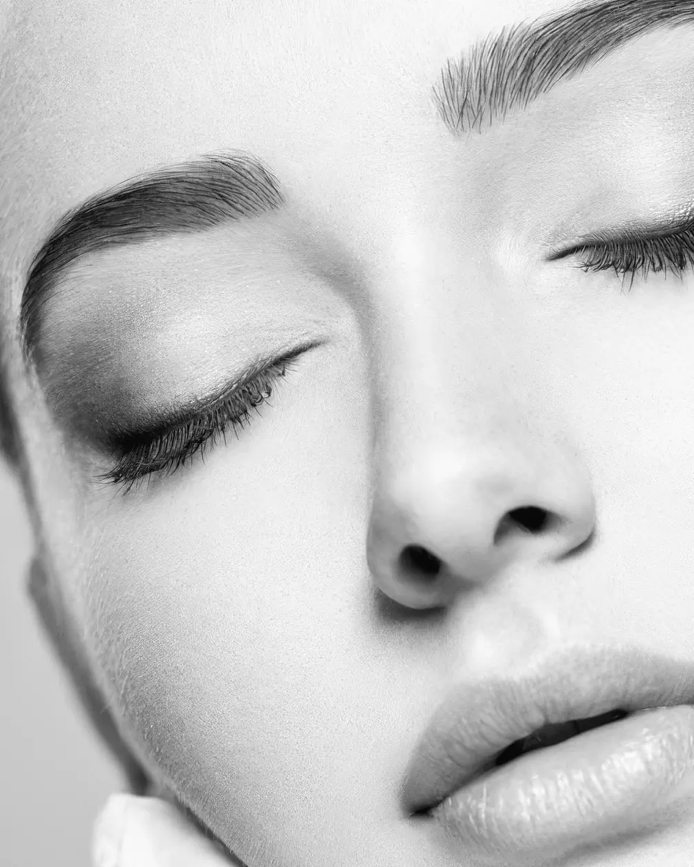 Occhi chiusi, il naso e le labbra: la pelle del viso da vicino, in bianco e nero